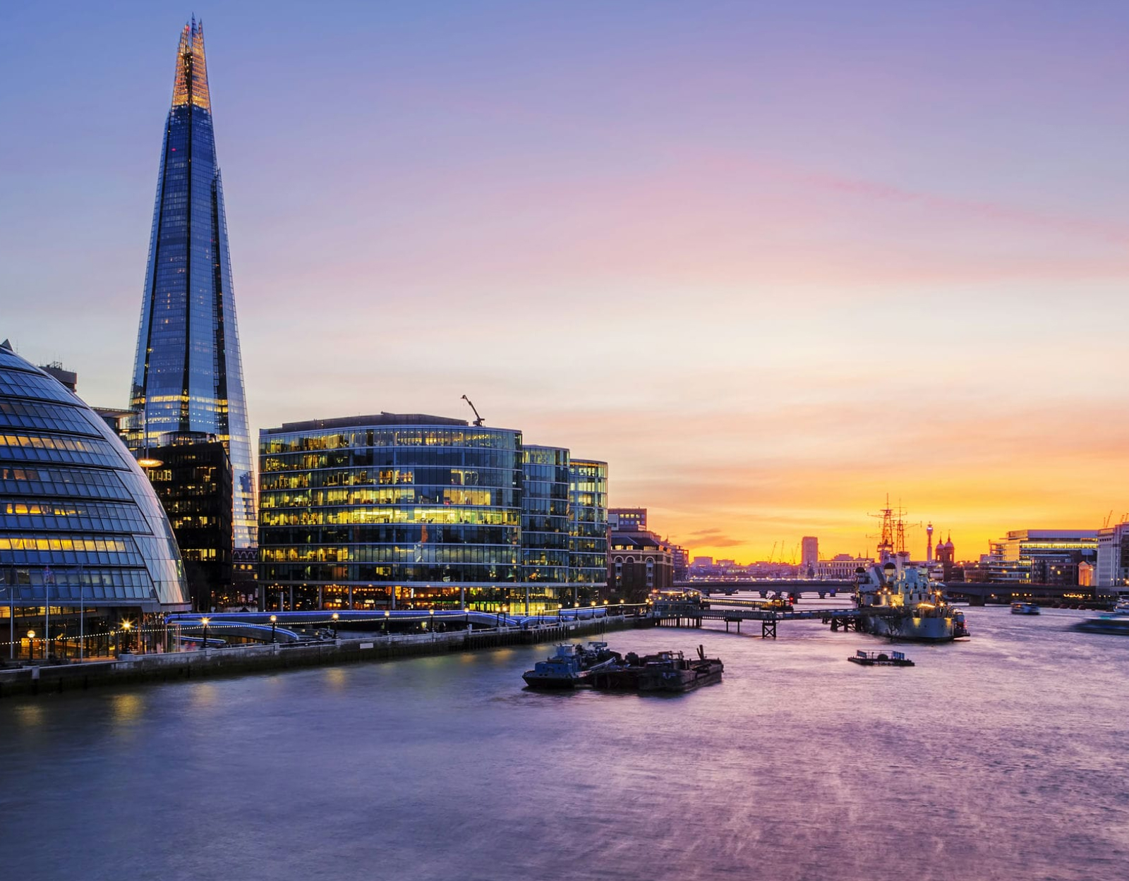 A view of a river, lined with commercial buildings, against a sunset