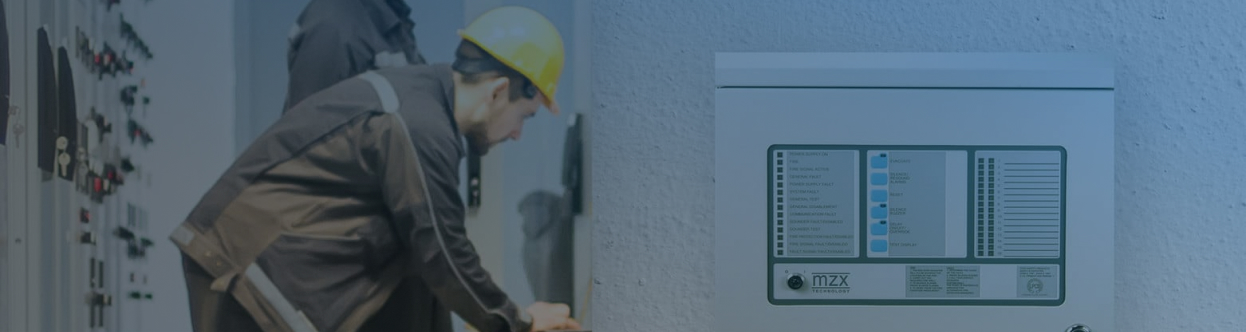 Two electrical engineers at work in a facility, with a fire control panel in the foreground