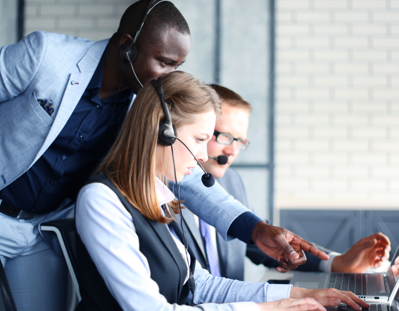 Two call center employees at work in an office, while another gives them instructions