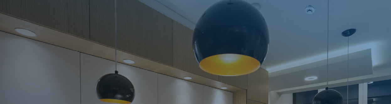 Fire detectors mounted on a ceiling near hanging lights